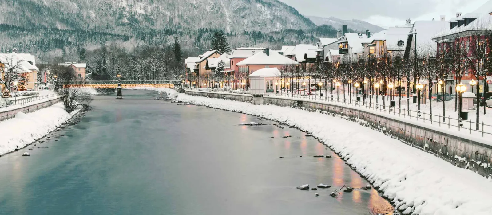 Die Ischl im Winter in Bad Ischl, flankiert von Häusern und warm leuchtenden Laternen