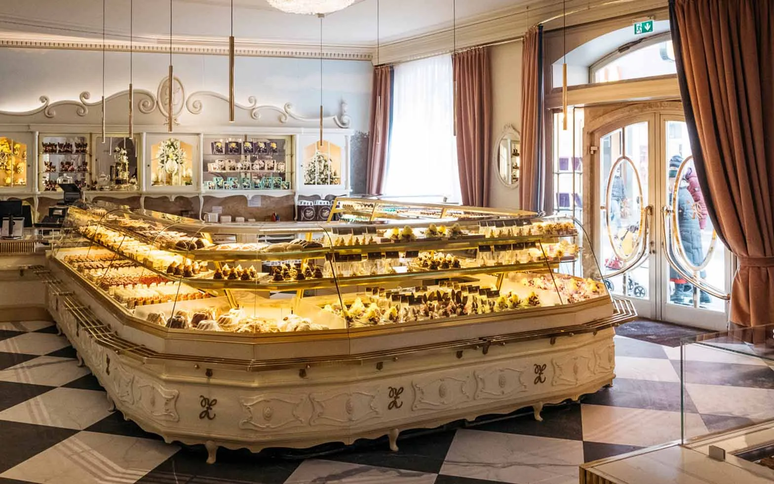 Elegante Konditorei Zauner mit großer, beleuchteter Vitrine voller Kuchen, Torten und Pralinen.