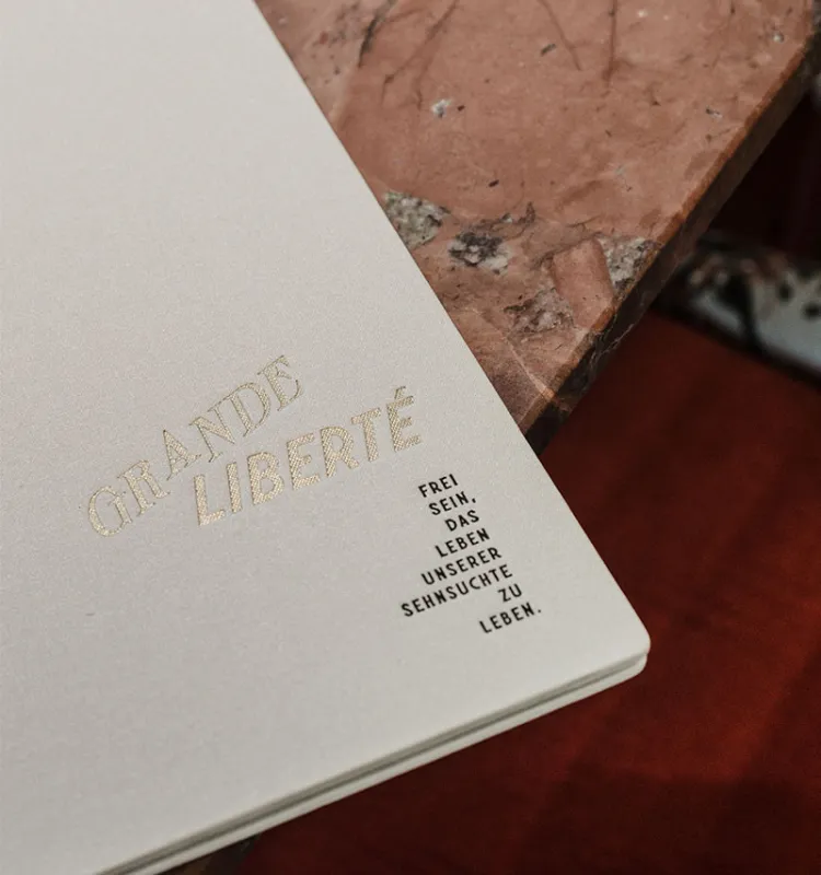 Speisekarte des Grande Liberté auf rotem Marmortisch mit goldener Prägung und Zitat