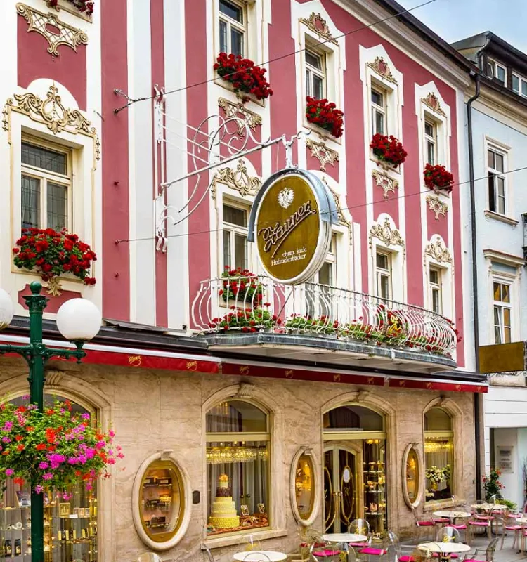 Historische Fassade der Konditorei Zauner in Bad Ischl mit roten Blumen und Außentischen