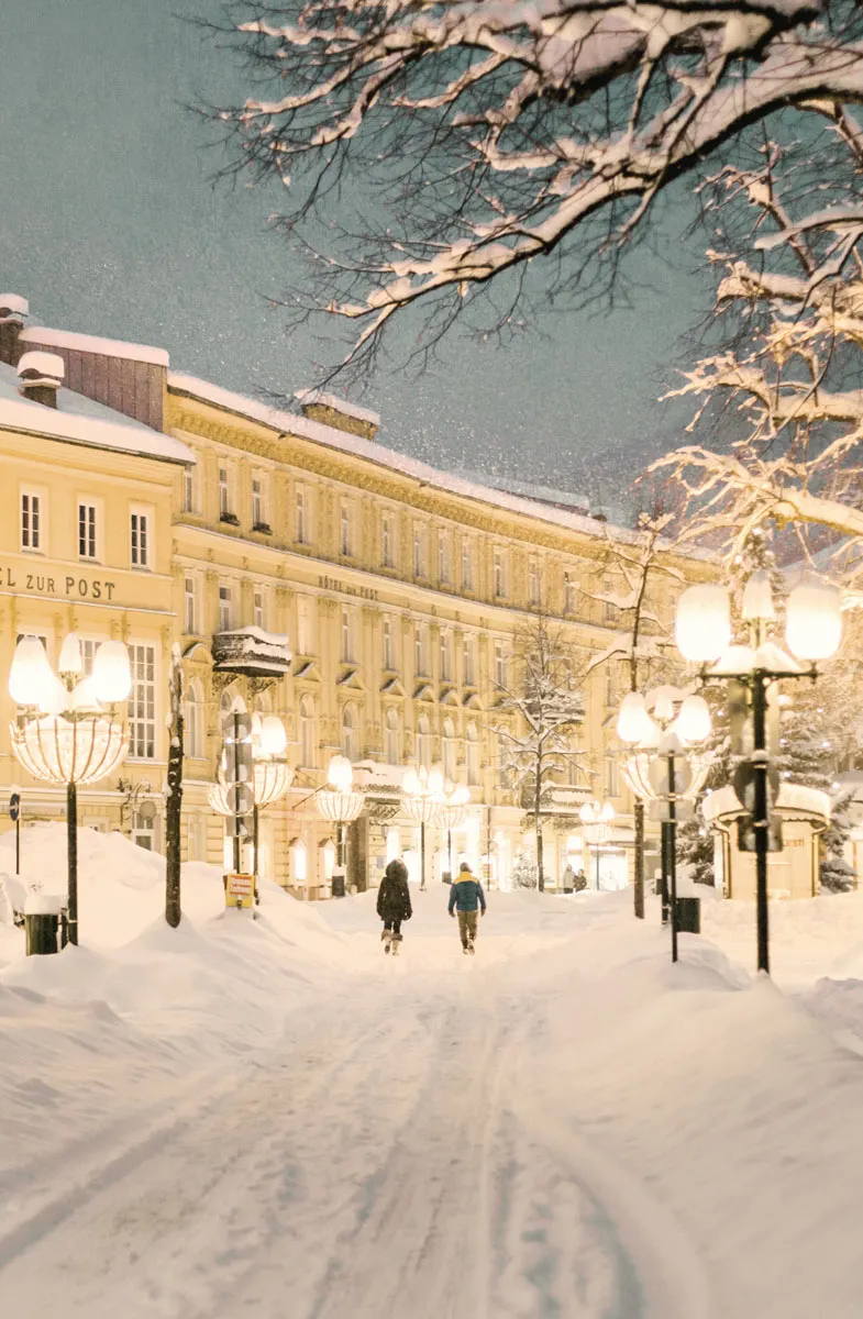 Schneepfad durch Bad Ischl, eingerahmt von Straßenlaternen und kunstvollen Hausfassaden im Hintergrund