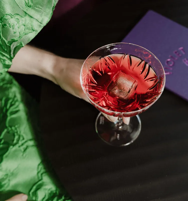 Cocktail mit Eiswürfel auf dunklem Tisch an der Hotelbar Violet Hour