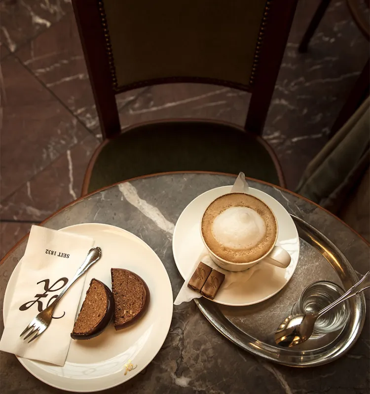 Cappuccino mit Wasser und Schokoladenkuchen auf einem Marmortisch in der Konditorei Zauner.