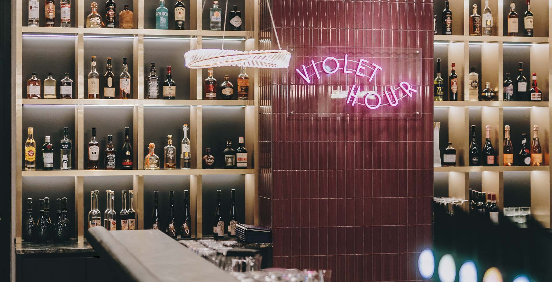 Elegante Bar mit Neon Schriftzug „Violet Hour" und Regalen voller Flaschen im Grand Elisabeth Hotel in Bad Ischl.