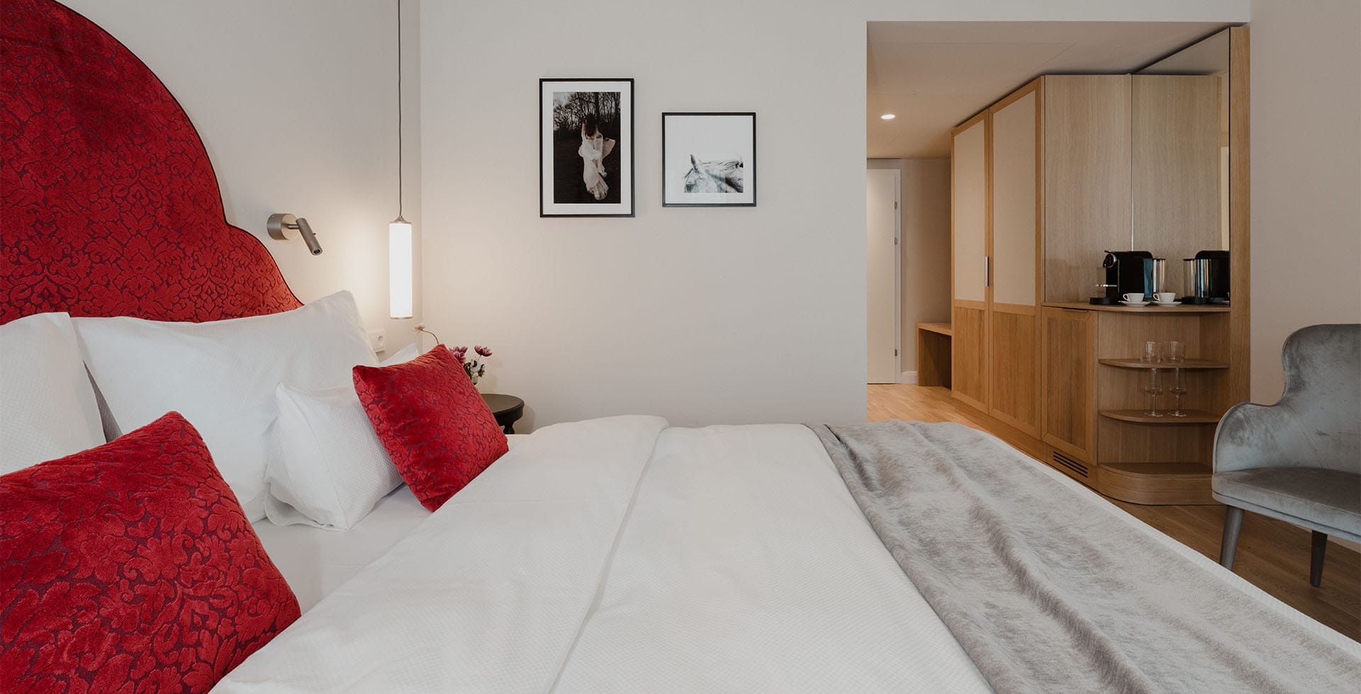 Innenansicht des Classic Doppelzimmers mit Balkon mit Bett, roten Zierkissen und Ausstattung im Grand Elisabeth Bad Ischl.