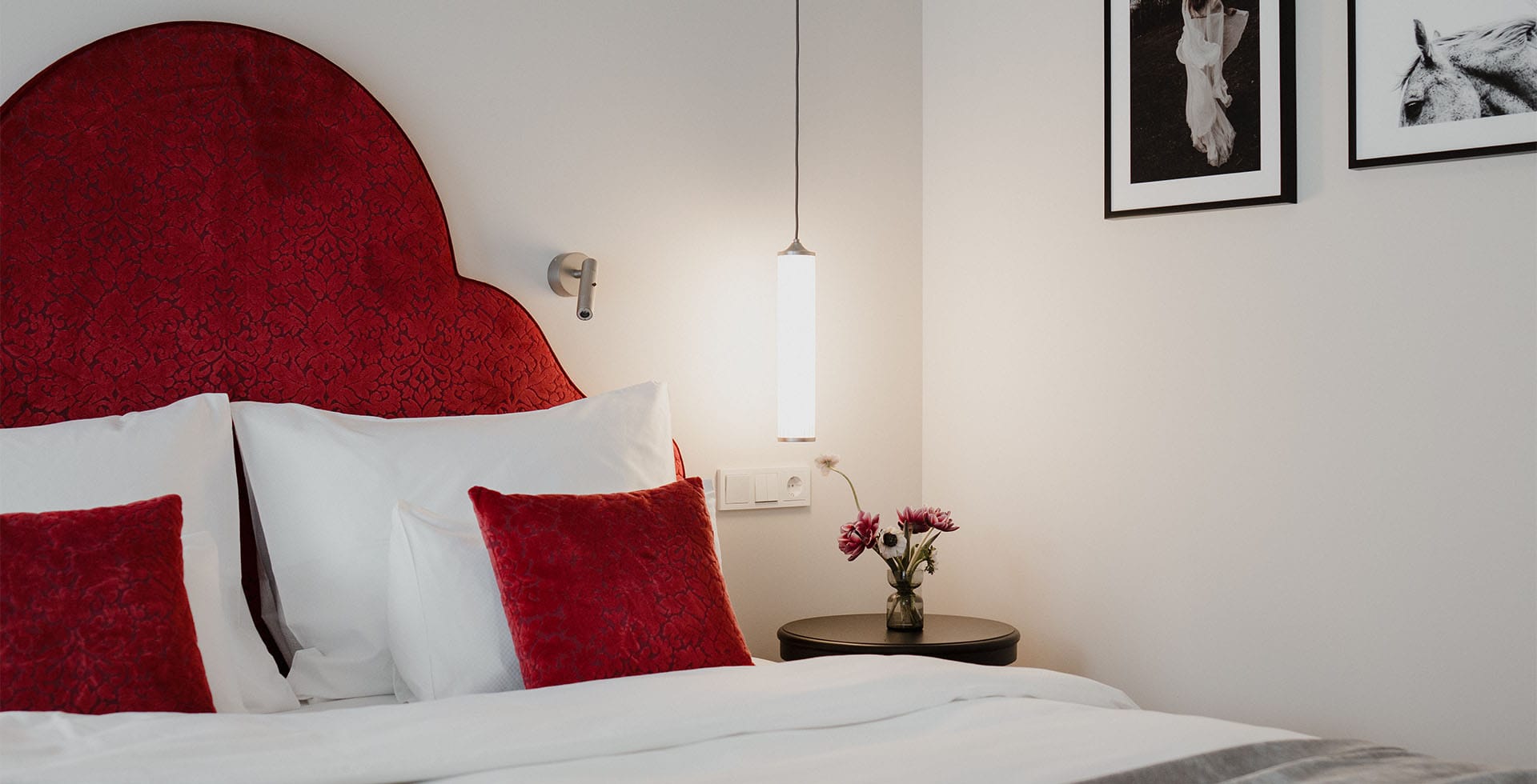 Classic Doppelzimmer mit Balkon, rotem Kopfteil, weißen Kissen, Nachttisch mit Vase und Wandbildern im Grand Elisabeth Hotel in Bad Ischl.