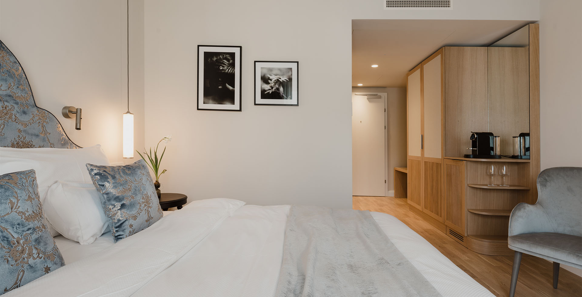 Innenansicht des Classic Doppelzimmers mit Bett, blauen Zierkissen, modernem Schrank und Kaffeemaschine im Grand Elisabeth in Bad Ischl.