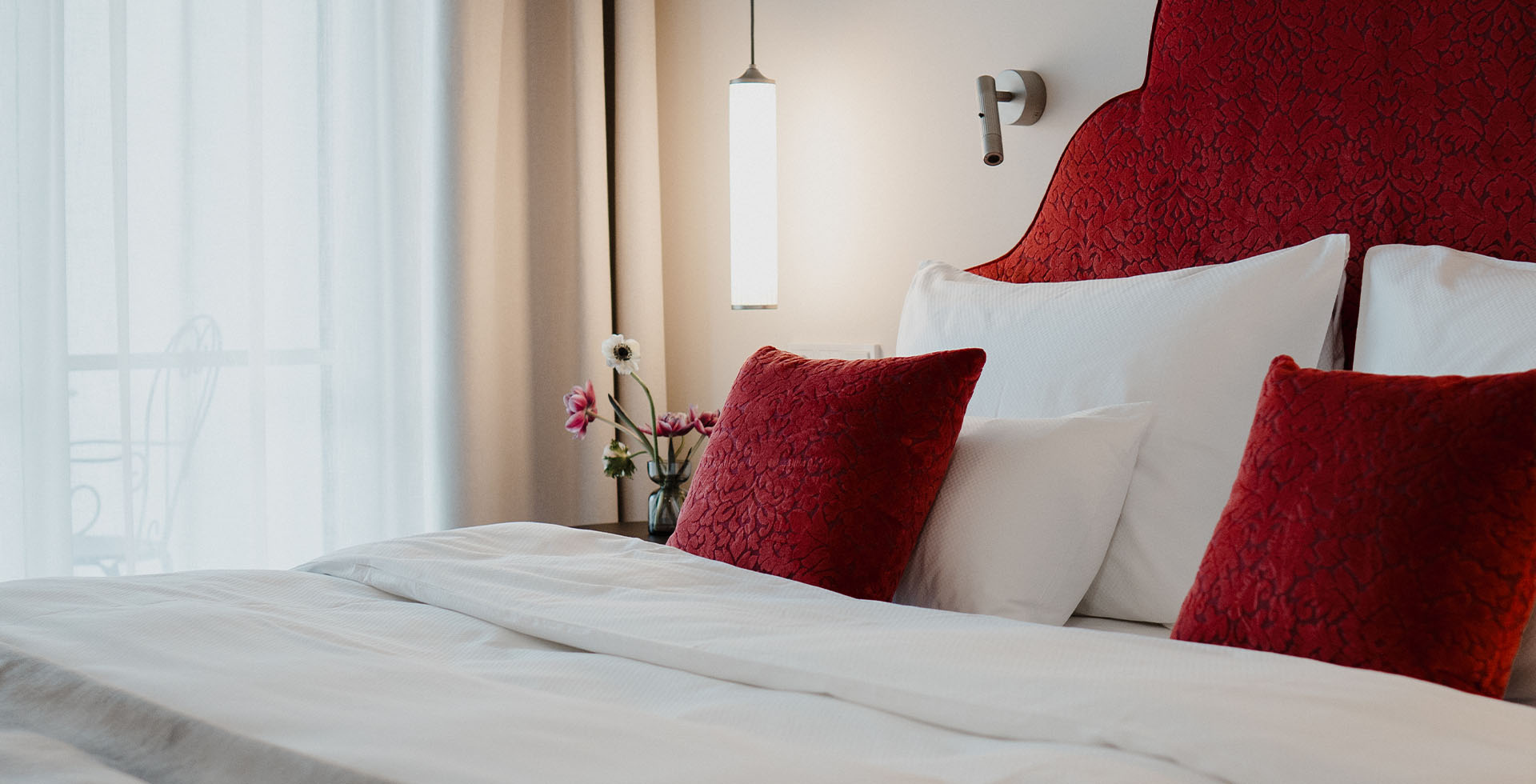 Großes Bett mit roten Samtkissen und weißer Bettwäsche im Designhotel Grand Elisabeth in Bad Ischl im Salzkammergut.