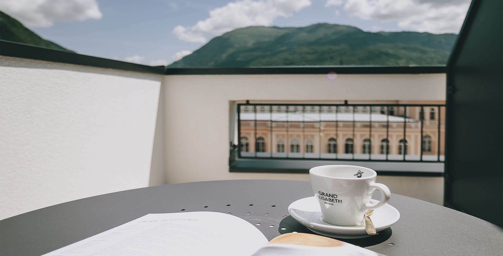 Eine Tasse Kaffee auf der Terrasse der Sisi Suite im Grand Elisabeth mit Aussicht auf Bad Ischl und die umliegenden Alpen.
