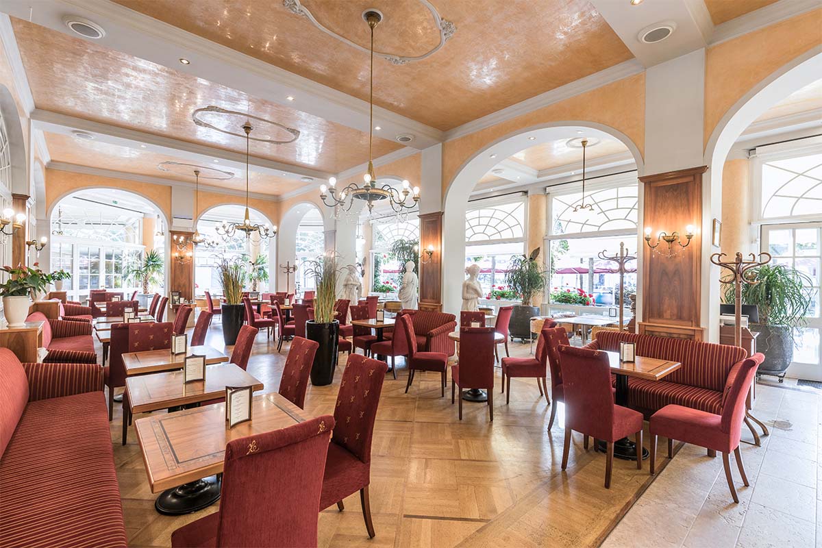 Heller Café-Sitzbereich mit roten Polstermöbeln, großen Fenstern und eleganter Einrichtung.