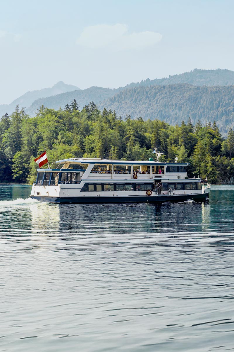Ein historisches Boot mit österreichischer Flagge gleitet über den Wolfgangsee, umrahmt von den Bergen des Salzkammerguts