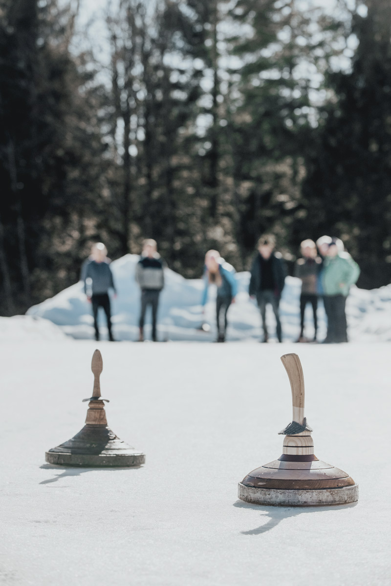 Zwei Eisstöcke gleiten über die Eisbahn in Bad Ischl, im Hintergrund eine zuschauende Gruppe