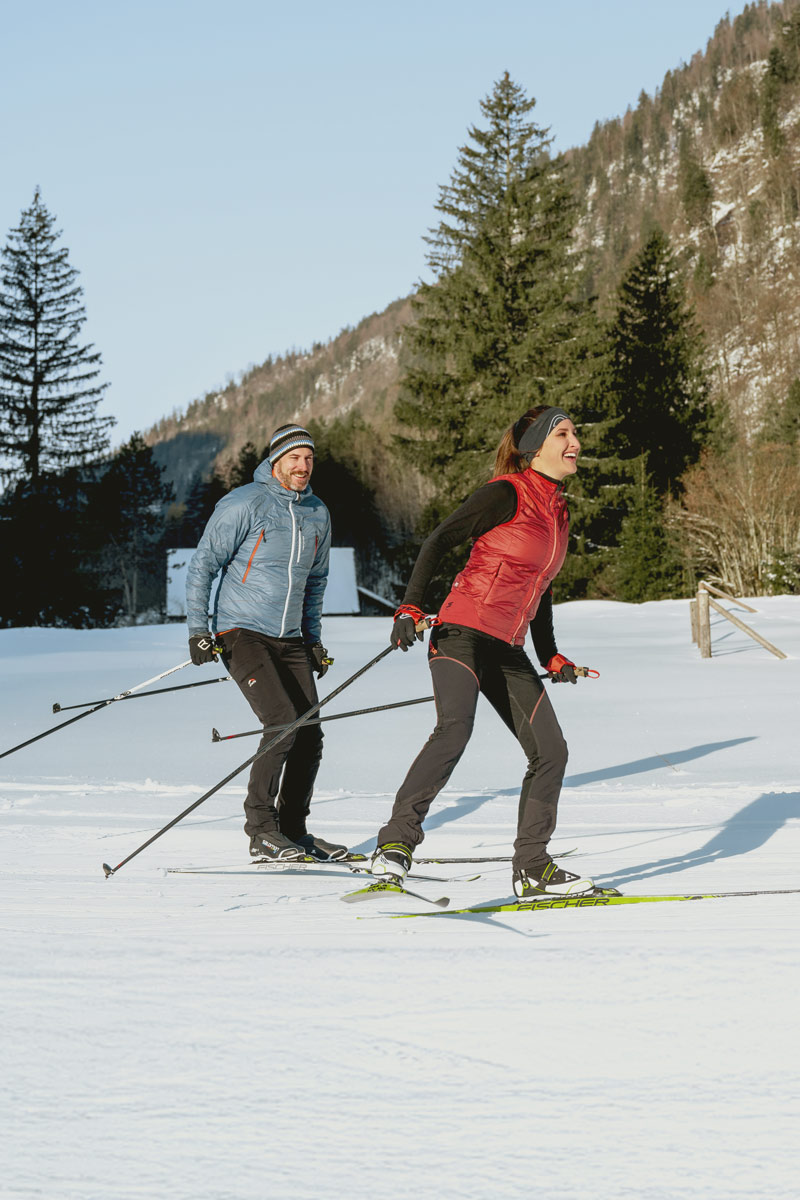 Ein Paar in winterlicher Kleidung gleitet auf Skiern durch den sanften Schnee des Salzkammerguts